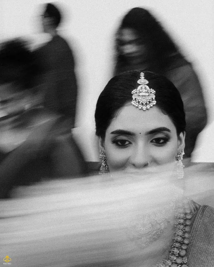 Black and white close-up of the bride in a maang tikka, framed through her veil