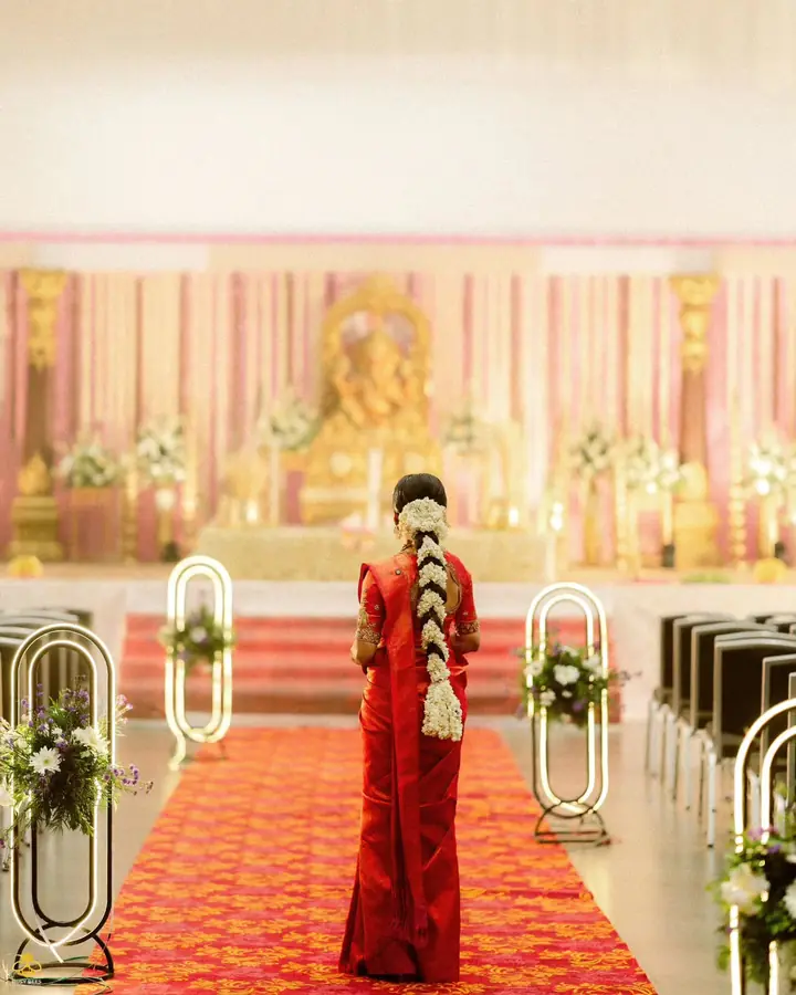 Bride in a red kanjeevaram walks the flower-lined aisle towards the mandapam