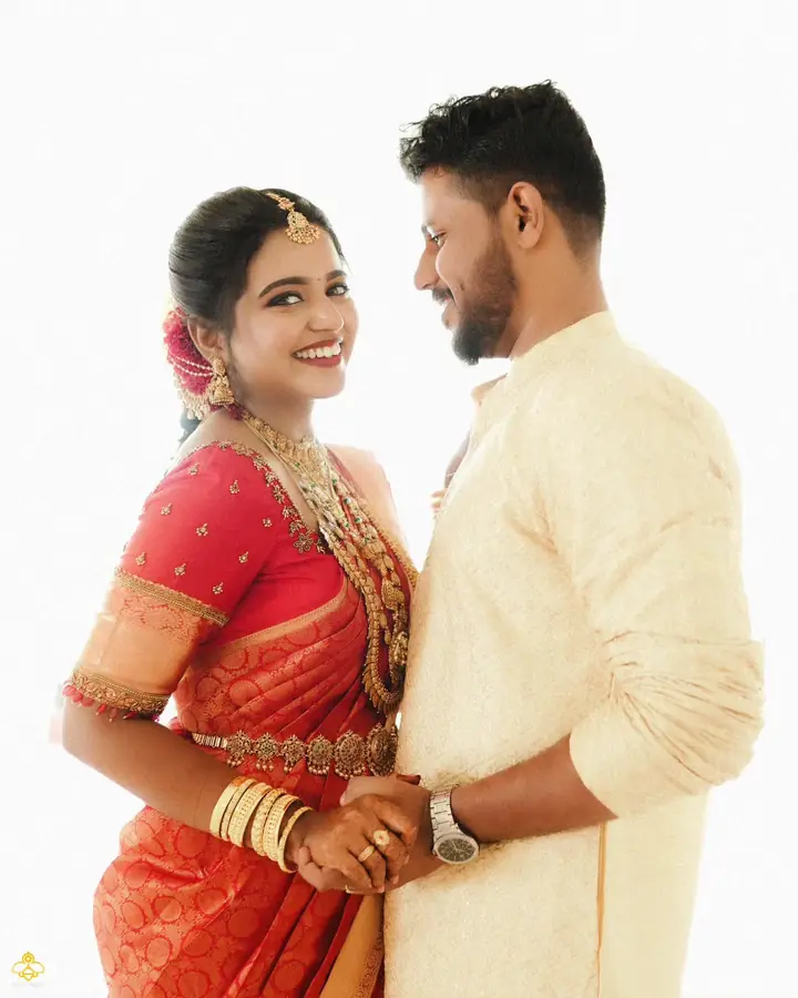 Bride in orange-red silk and groom in cream, looking at each other