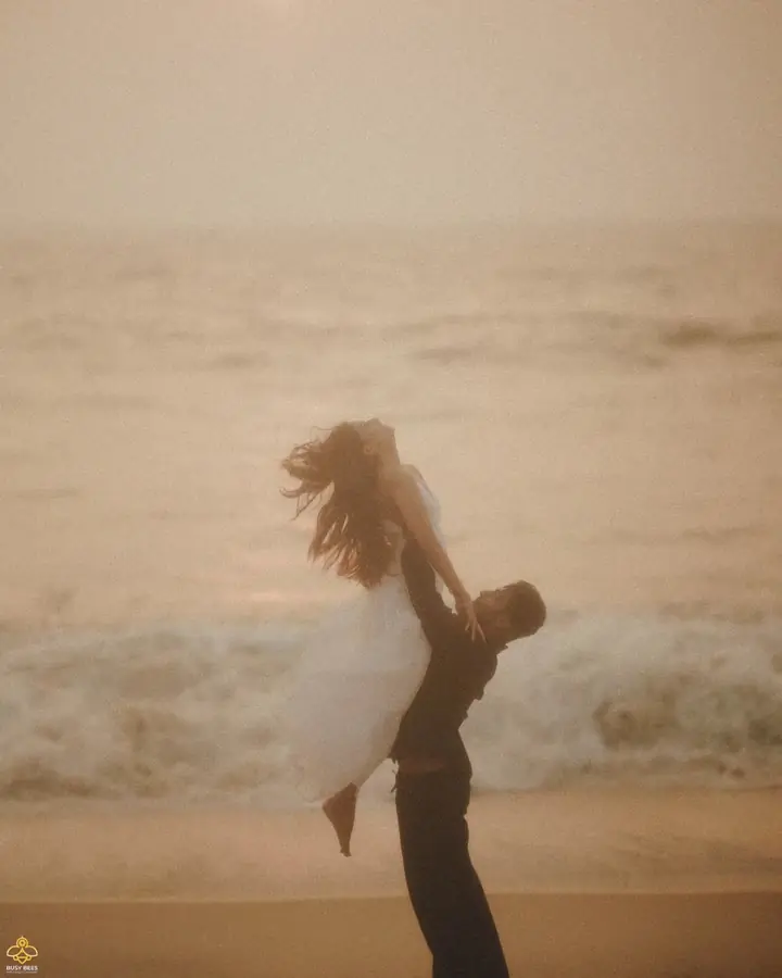 Groom lifts the bride at the water's edge on a Kerala beach at dusk