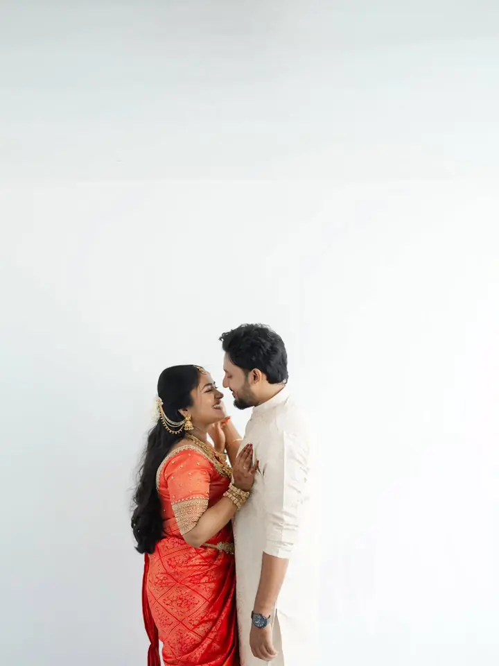 Bride in red and groom in cream face each other against a bright white wall