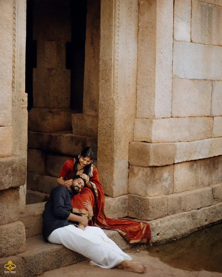 Couple resting against carved stone pillars at a ruined temple mandapa