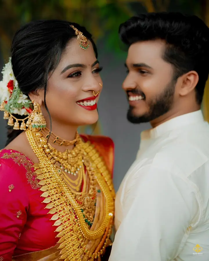 Bride in layered temple gold and a pink blouse smiles at the groom