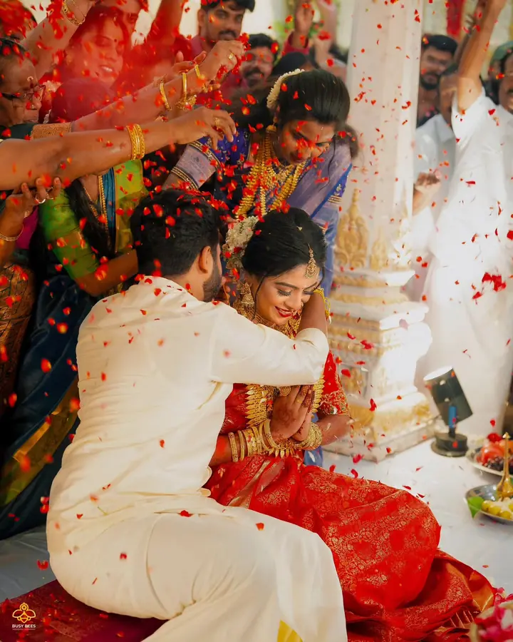 Family shower the seated couple with rice and red petals during the ceremony